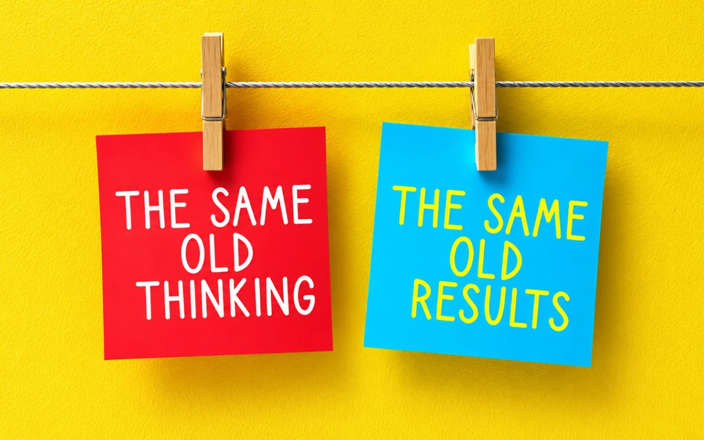 Two sticky notes pegged to a line on a yellow wall: a red one reads “The same old thinking” and a blue one reads “The same old results”.
